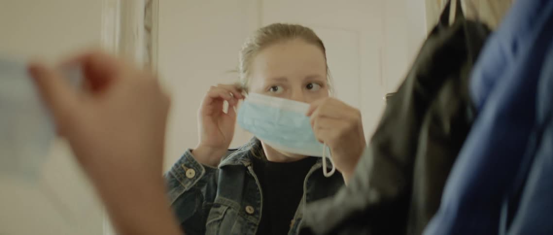A teenager puts her coat on and then a mask
