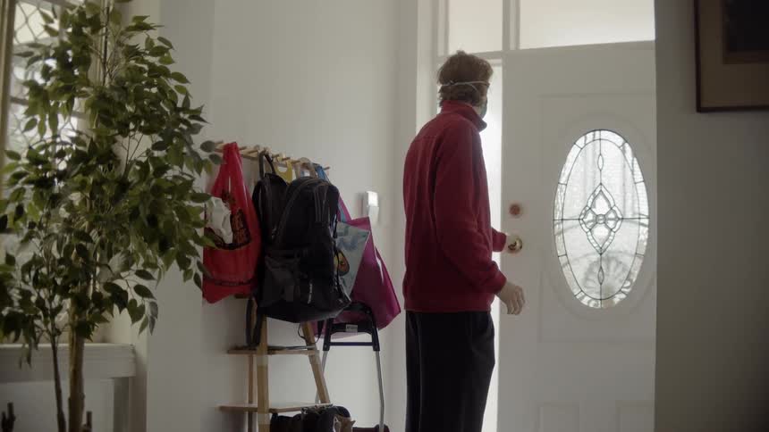 Male places face mask on and straightens his hair with his hands before opening the front door and leaving the house