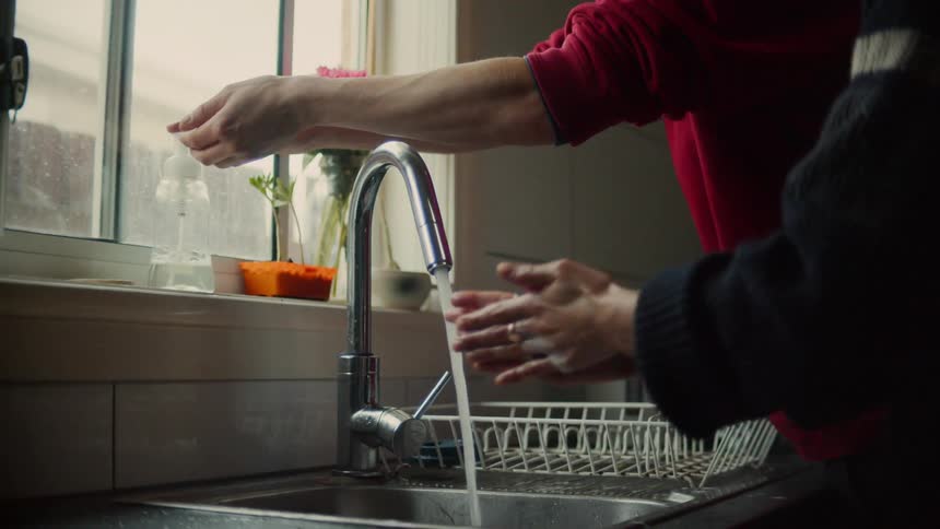 A pair of people soaping up their hands in front of a running faucet