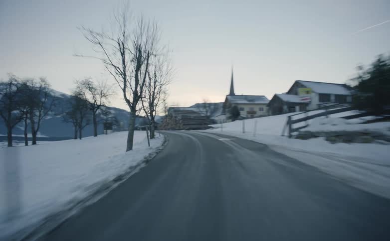 A vehicle travels a rural county road with a few houses passing by