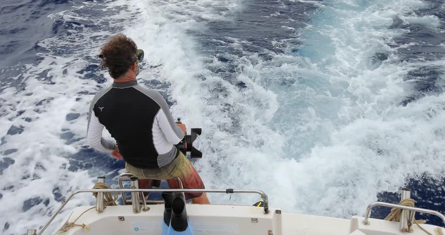 A man holding onto a camera and balancing on the back of a boat as the boat travels