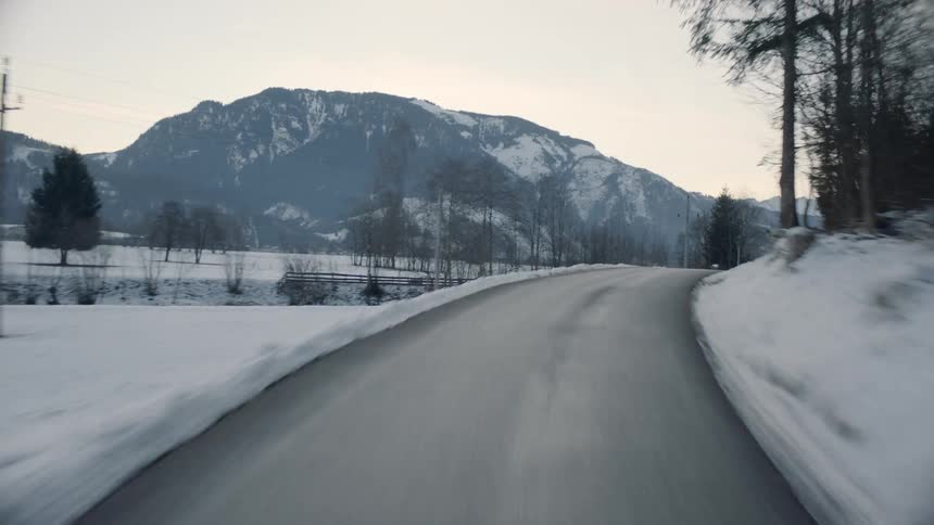 Vehicle drives along winding narrow road in the snowy hills