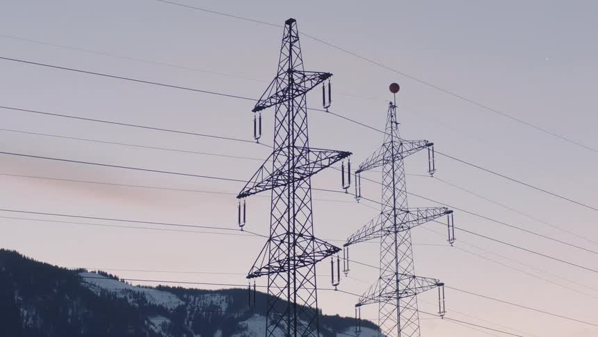 Two power towers with electrical lines against the sky with mountain ridge behind