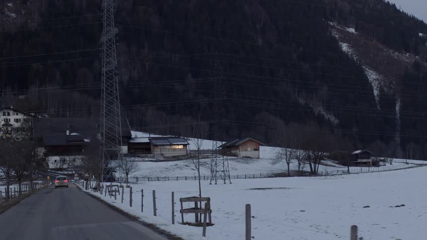 A vehicle driving on a road with houses and a mountain on the foreground