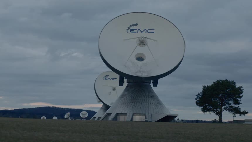 Radio telescopes stand in field with mountains and buildings on the horizon