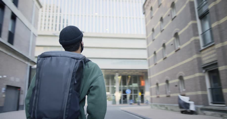 A man wearing a face mask walks toward an office building in a city