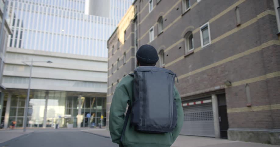 Male carrying a backpack walks down the middle of the street in a deserted city