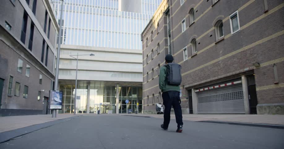 Male wearing a backpack walks down the middle of the street in a deserted city
