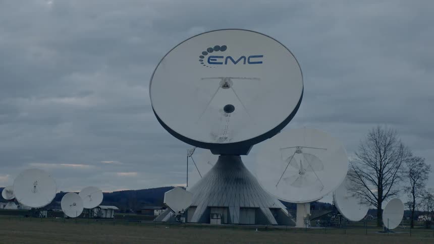 Several satellite antenna stand in a grassy area on a cloudy gray day