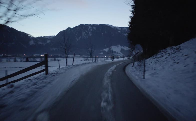 Vehicles drives along winding narrow road in the snowy hills at dusk