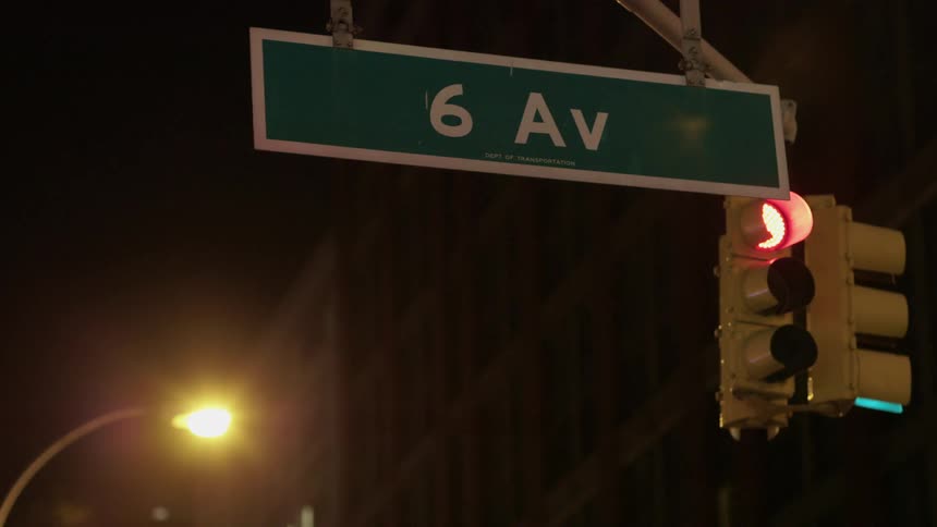 Street sign hangs next to traffic light near building at night