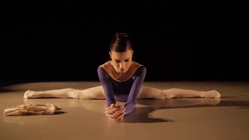 A ballerina stretches on the floor