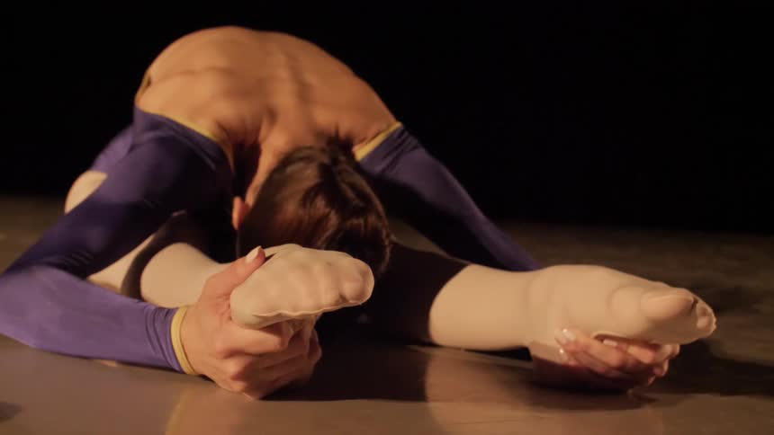 A dancer bends over her legs and stretches