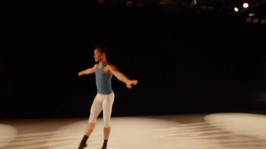 Male ballet dancer leaping across the stage under spotlights