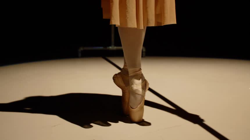 A woman in a skirt dances in cream colored ballet shoes