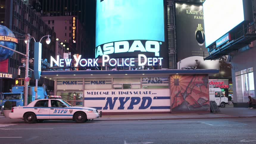 A police car is parked in front of the times square police substation at night