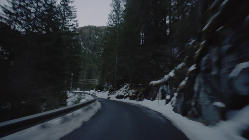 Vehicle drives along winding narrow road in the snowy mountains
