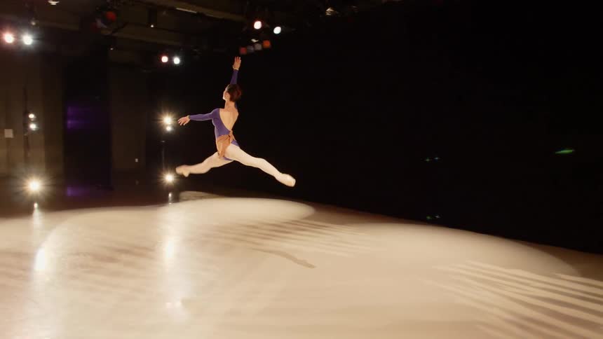 Ballet dancer leaping across the stage under spotlights