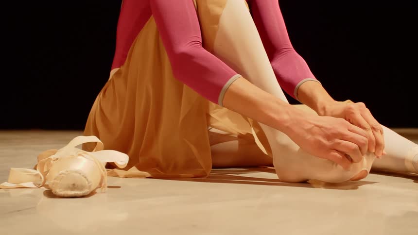 Ballet dancer sitting on floor stretching her foot before performing