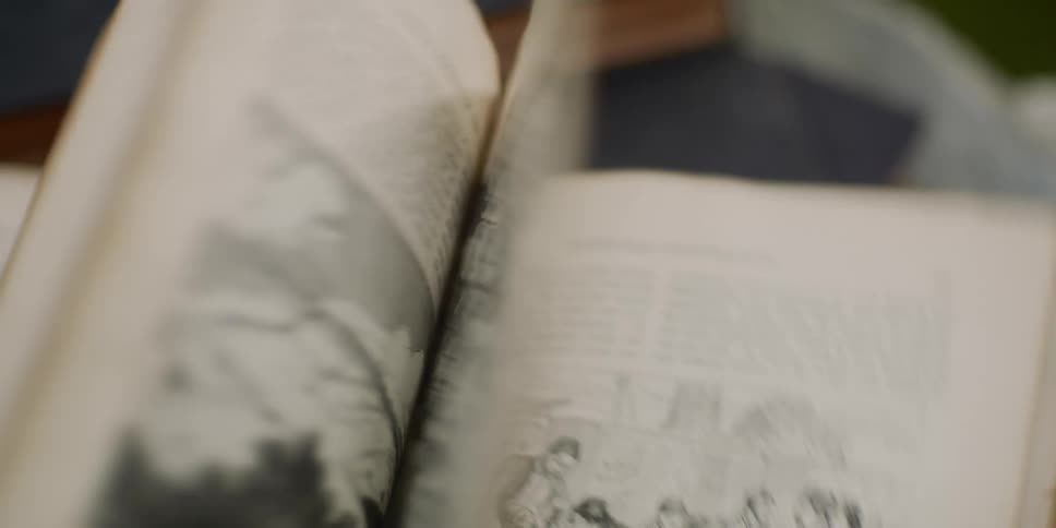 Someone sitting at a desk quickly flips through pages of a book filled with text and black and white drawings