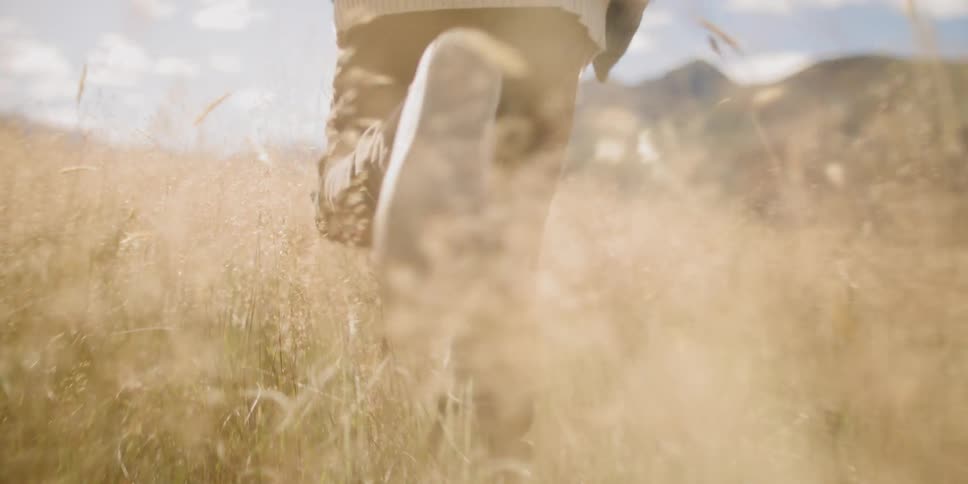 A person running through a grassy field with mountains in the distance