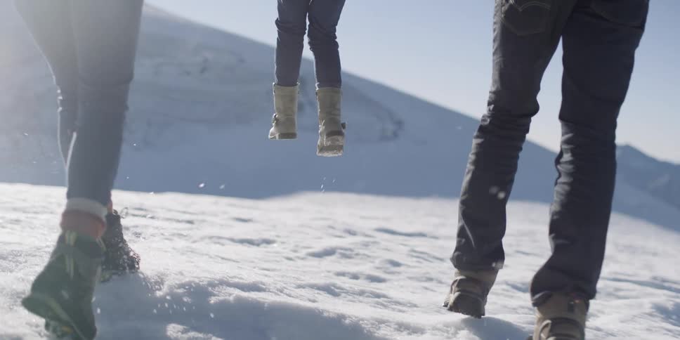 A mother and father lift their daughter up playfully in the snow