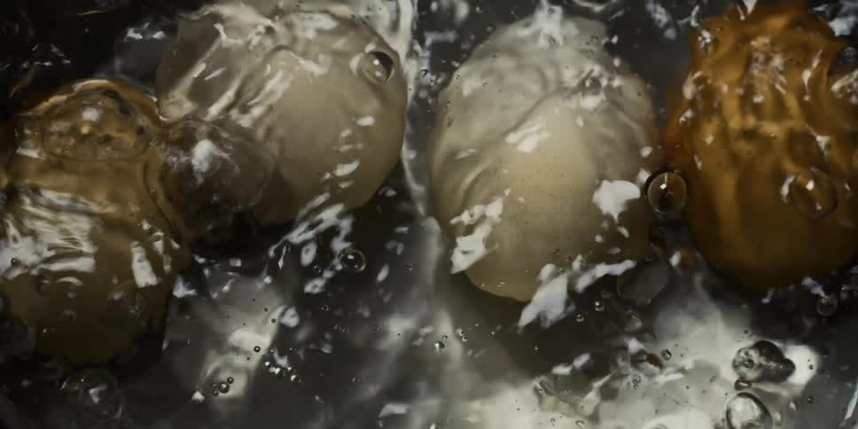 White and brown eggs in their shells cook in the boiling water