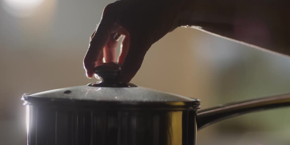 A person lifting a pot lid to release steam from a pot