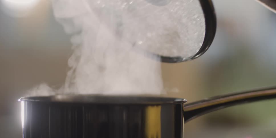 Person removes a lid from a pot of steaming contents