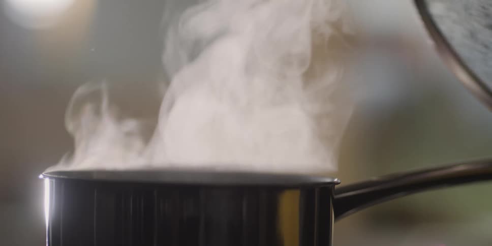 A hand lifts the lid of a pot and the replaces after releasing steam