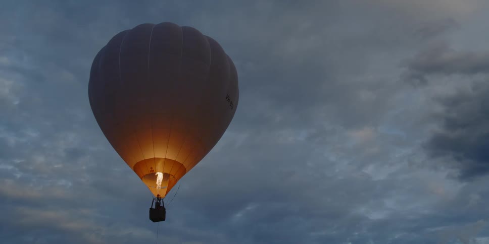 A hot air balloon floats and starts to rise as flames burst from the burners