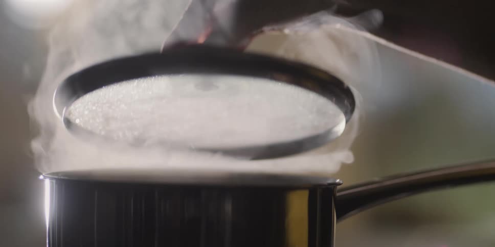 Hand lifting steaming lid on a pot that is cooking