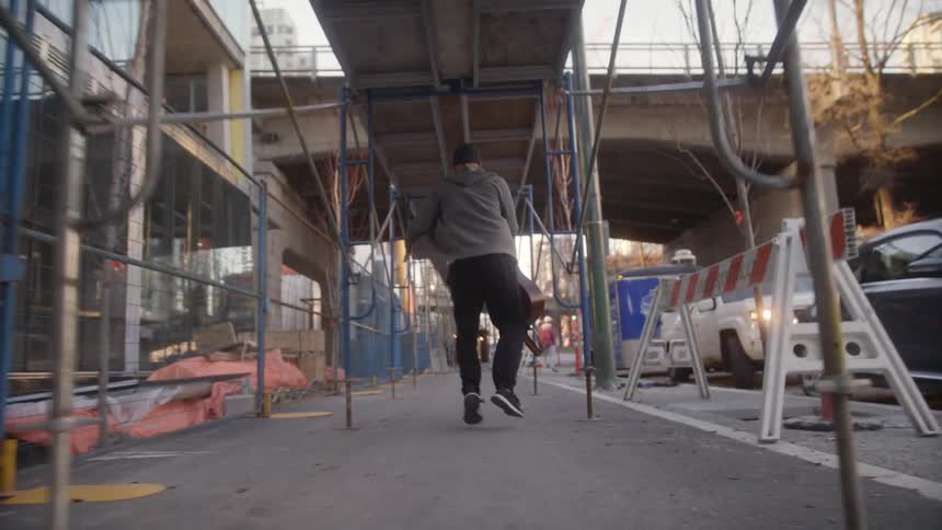 Man carrying a guitar runs along the pavement in the city