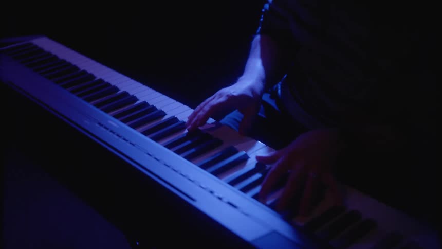 Person playing on keyboards in the darkness on stage
