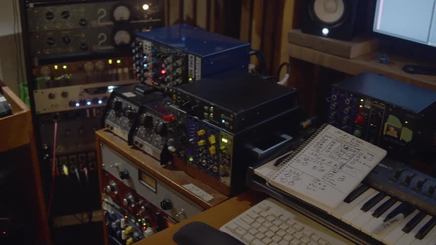 A person stands in a room filled with electronic music equipment