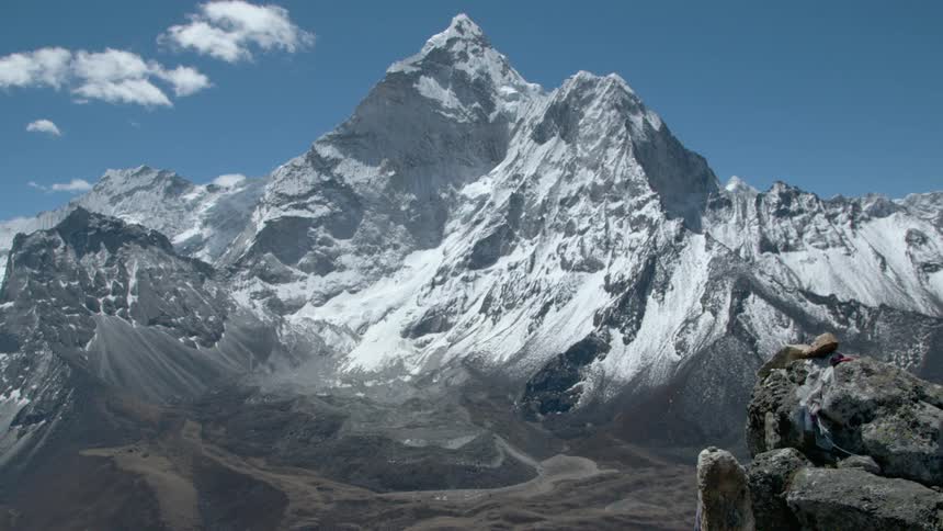 A piece of fabric on a ledge blows in the wind the a jagged mountain ridge against a bright blue sky