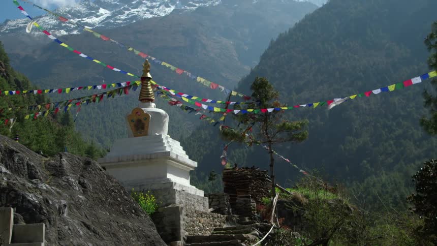 Colorful prayer flags strung to a temple in the wind at the base of a mountain