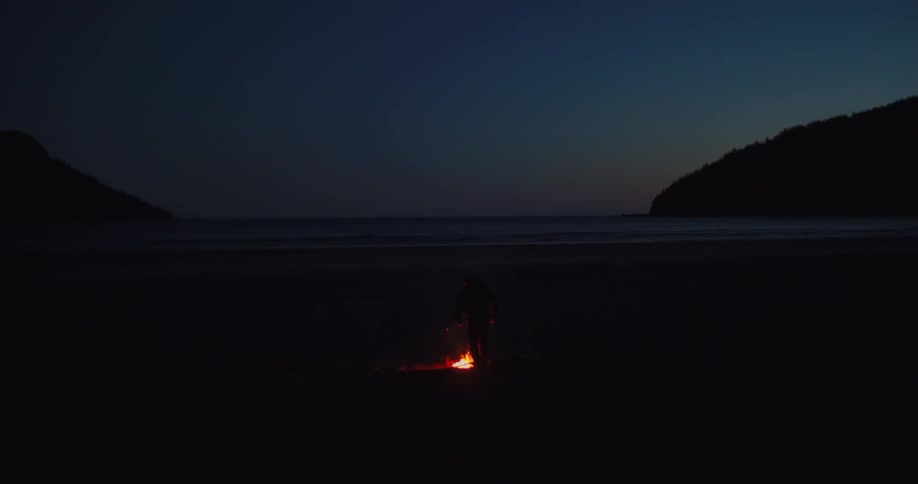 A man builds a campfire on the beach at night