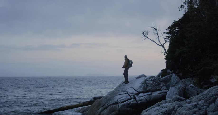 A man walks across rocks and take a picture of the water