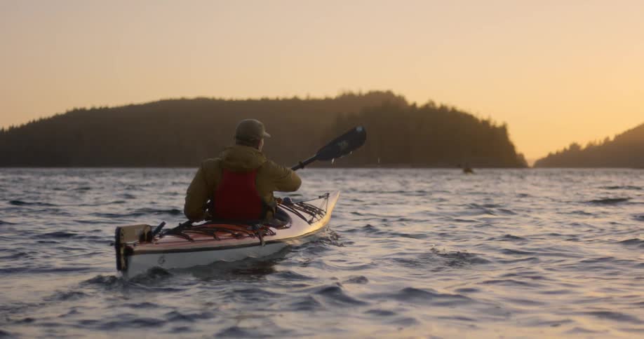 Man paddling in a canoe towards small island at sunrise