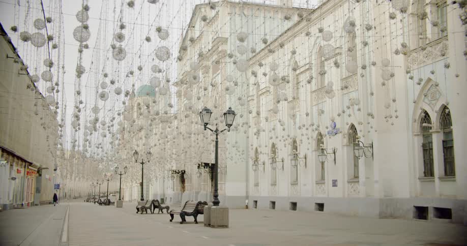 White lanterns and ornaments hang from wire covering an empty plaza with one person walking in the distance