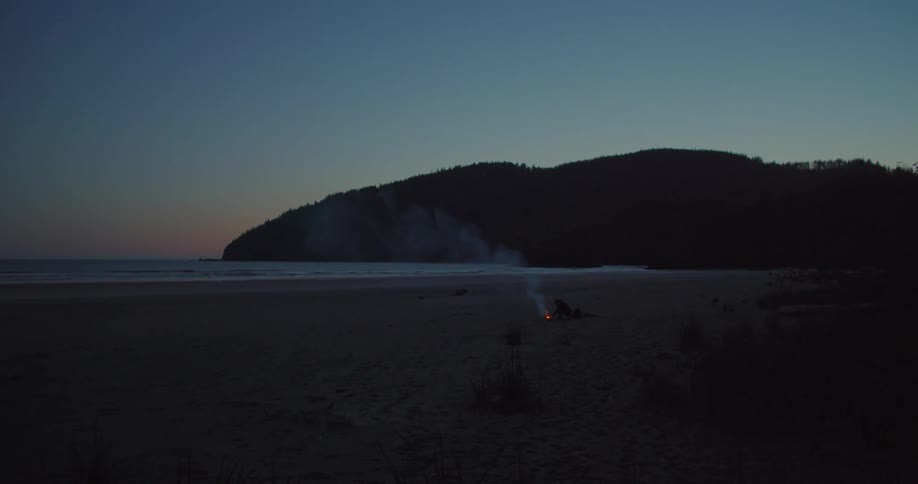 Man builds a fire on the beach at dusk