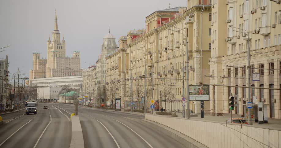 A few cars and a couple of people on a wide multi lane street with large buildings in a city that looks deserted