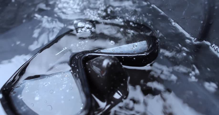 Water splashing down upon, and over, a pair of diver's goggles