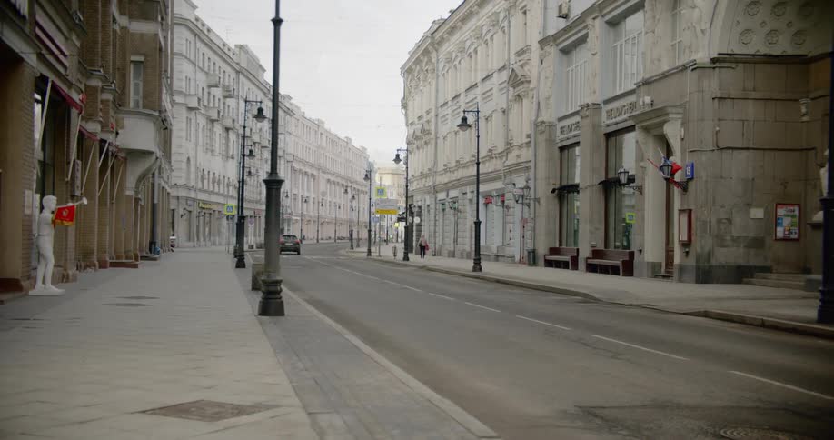 Car drives down empty street past ornate buildings and shops