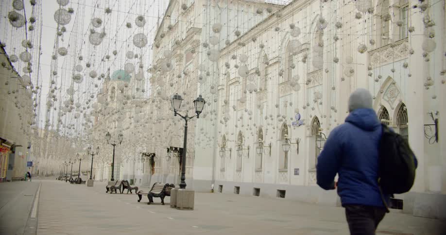 A young man with a backpack walks through an empty courtyard covered with hanging lanterns and ornaments