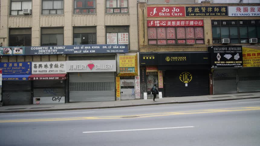 Male carrying a duffel bag walks swiftly along a sidewalk in a deserted city where all of the businesses are closed down