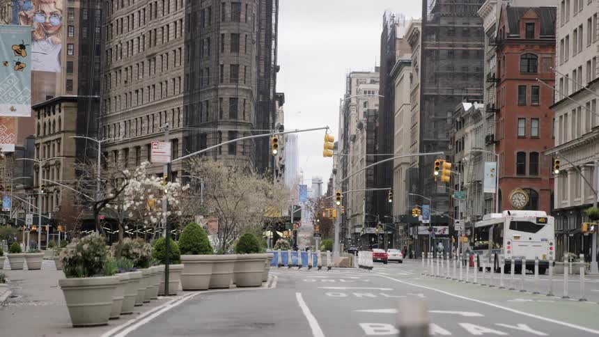 Traffic traveling along a street between rows of tall buildings in a city during the day