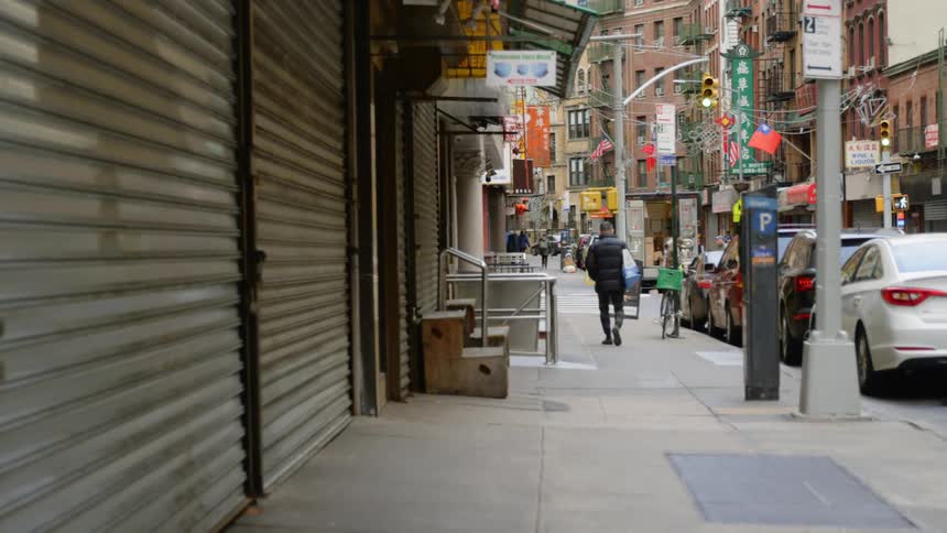 A man walks down the sidewalk in chinatown past shuttered and closed store fronts