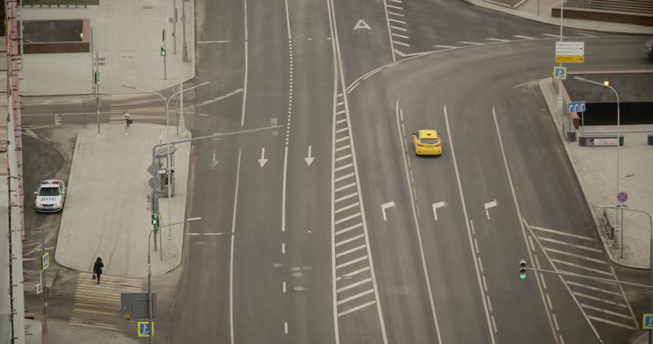 A taxi cab makes the turn on a practically empty city street with only two pedestrians on the sidewalk